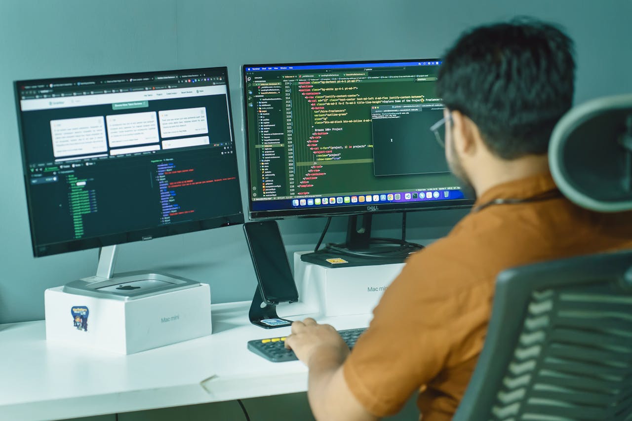 gallery-03 A software developer engaged in coding on dual monitors in a modern office setting.